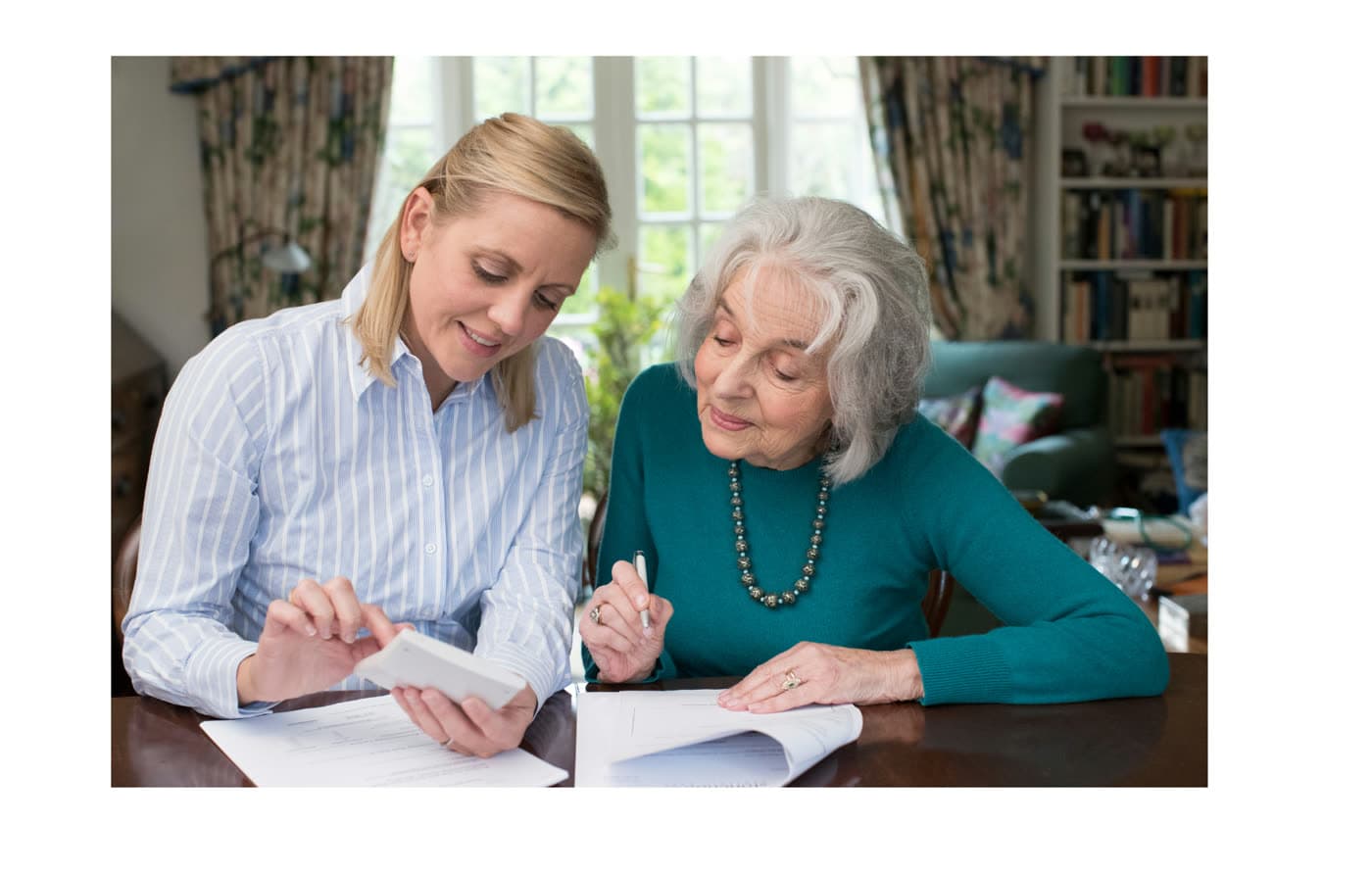 A caregiver journaling beside an older woman at the table